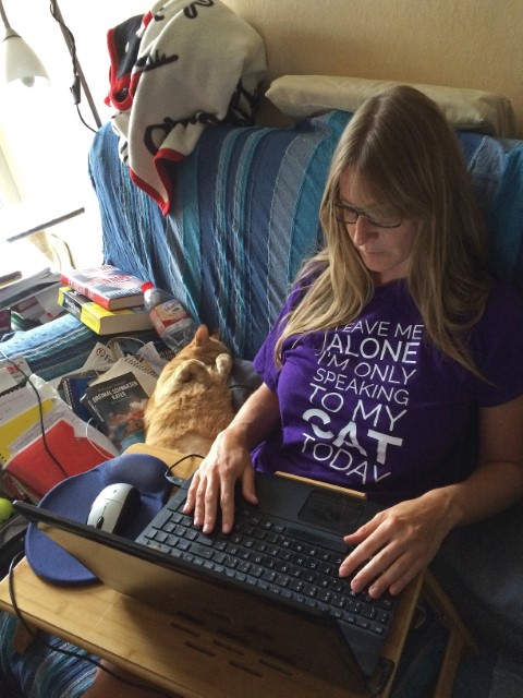 Junge Frau schreibt am Laptop neben schlafender Katze