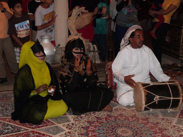 Frauen und ein Mann mit Trommel sitzen in einem Zelt in Oman und unterhalten Touristen