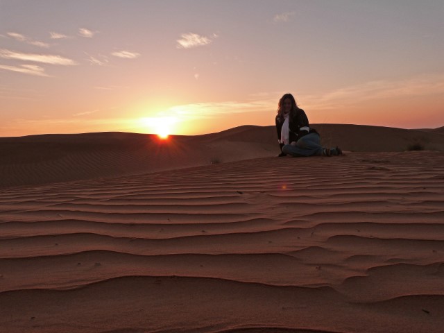 Junge Frau sitzt bei Sonnenaufgang in der Wüste in Oman