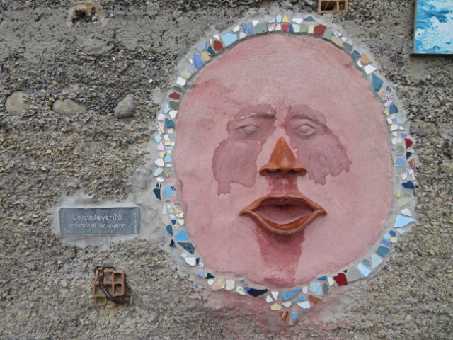 An der Mauer von Bussana Vecchhia findet sich Kunst wie dieses runde rosa Gesicht mit großem Mund